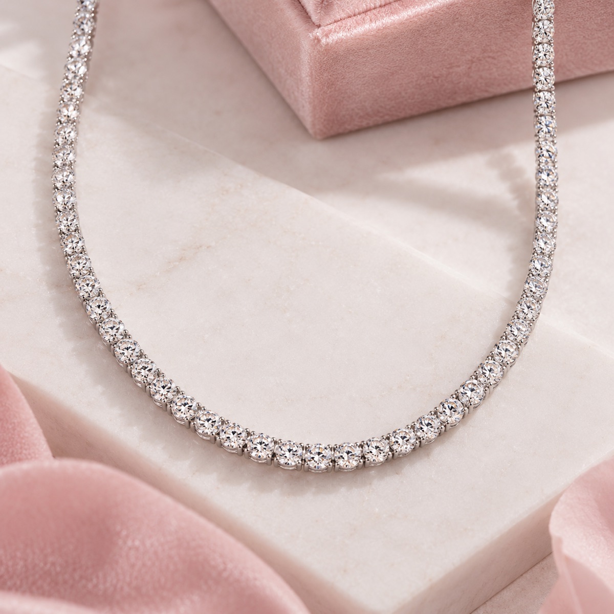 Diamond tennis necklace laid on marble with a pink velvet box